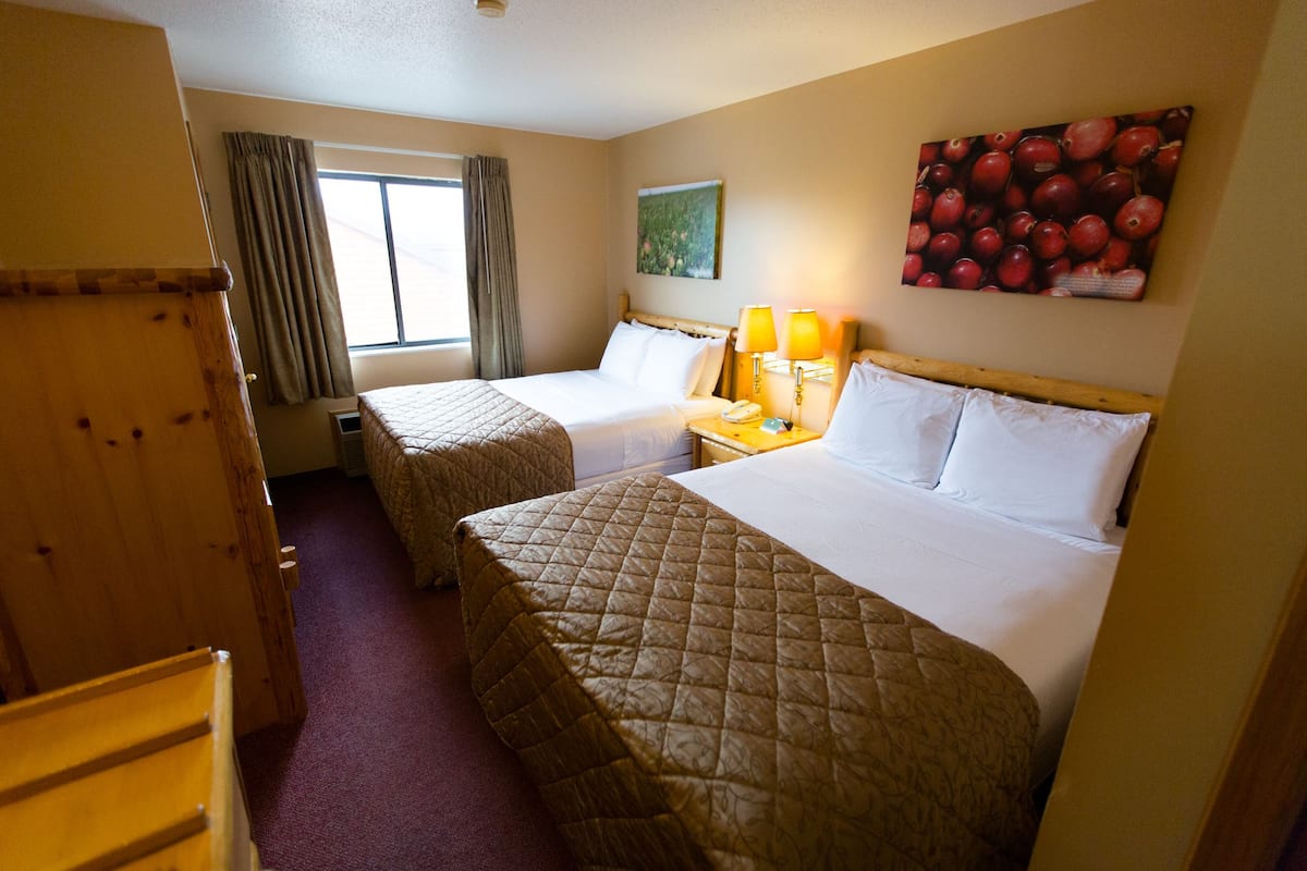 Een hotelkamer met twee bedden, een houten garderobe, een raam met gordijnen, een bedlampje en een schilderij van bessen aan de muur.