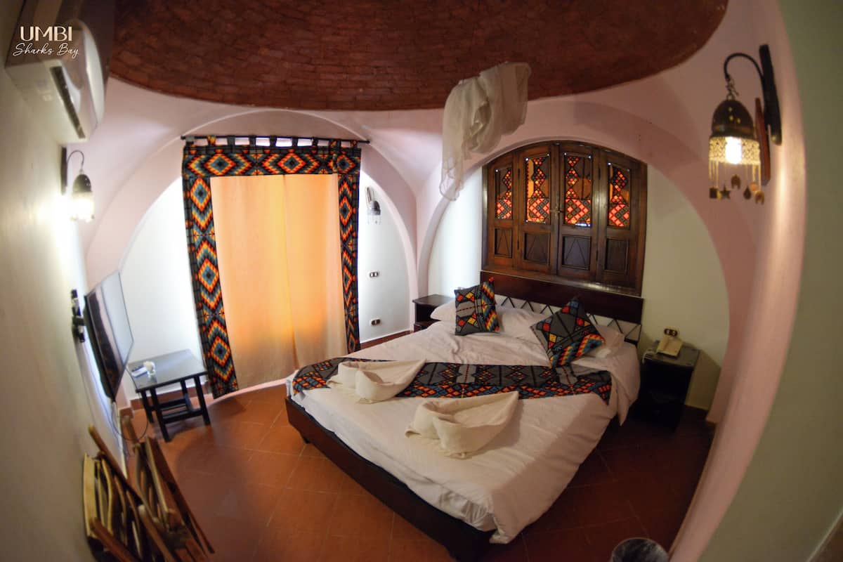 Ein Schlafzimmer mit einem großen Bett, einem hölzernen Kopfteil, einem Nachttisch, einem Fernseher und einem gemusterten Vorhang.