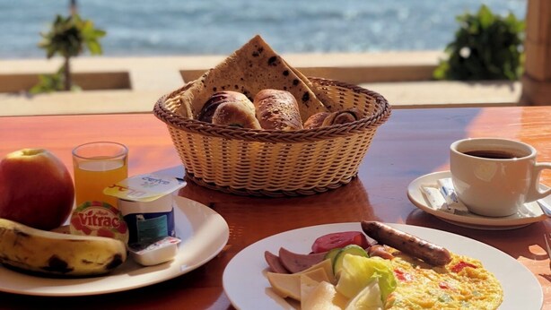 A breakfast table with a basket of bread, a plate of eggs, and a cup of coffee, overlooking the ocean. - Umbi Sharks Bay Diving Village (Sharm El Sheikh)