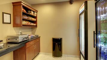 A kitchenette with a microwave, a trash can, and a refrigerator stocked with beverages.