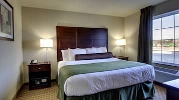 A hotel room with a large bed, two bedside tables, a nightstand, a window with curtains, and a framed picture on the wall.