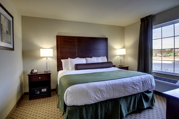 A hotel room with a large bed, two bedside tables, a nightstand, a window with curtains, and a framed picture on the wall.