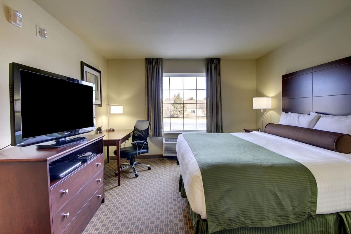 Une chambre d’hôtel comprenant un lit, un bureau avec une chaise, une télévision, une commode et une fenêtre avec des rideaux.