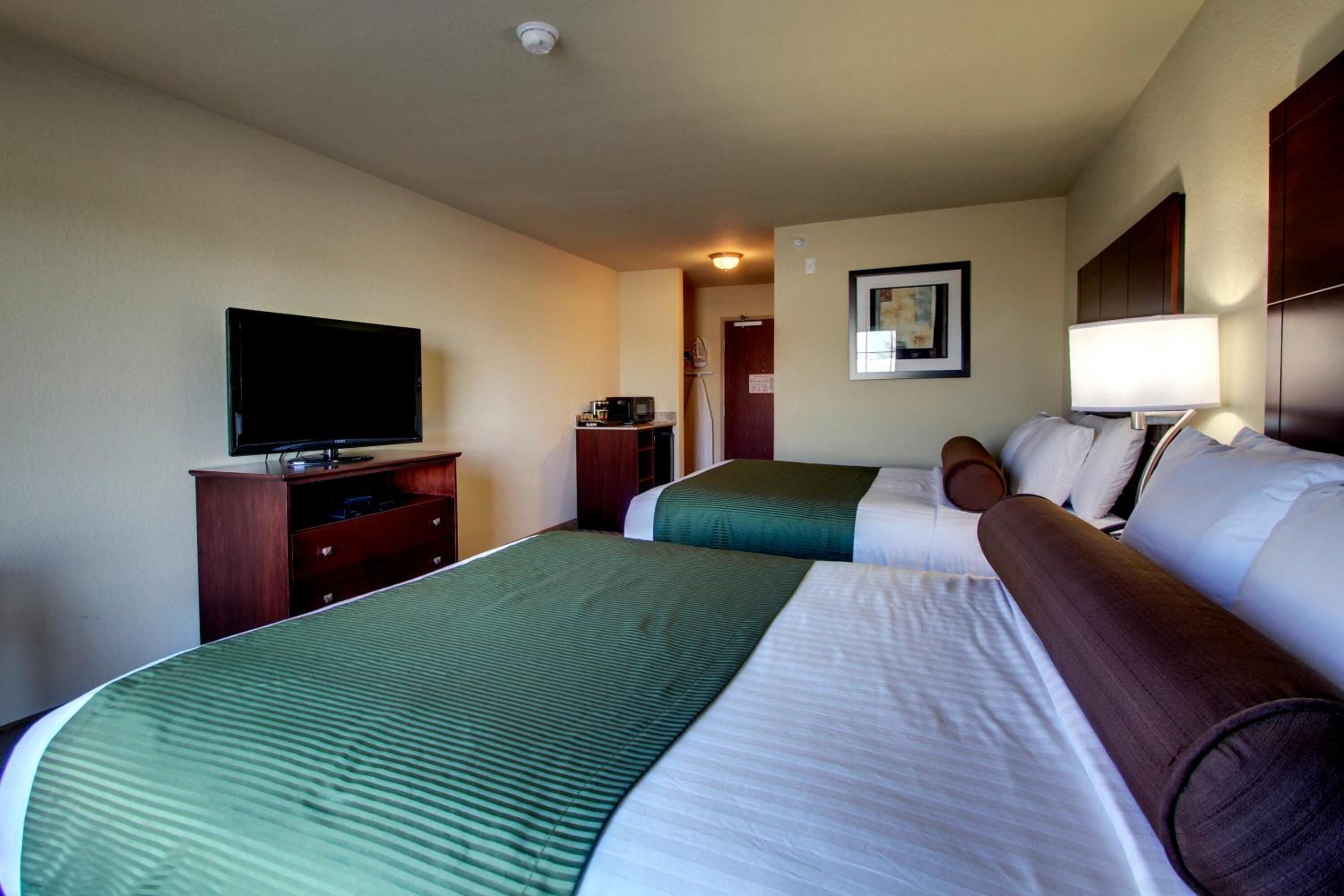 A hotel room with two beds, a TV, a desk, and a lamp.