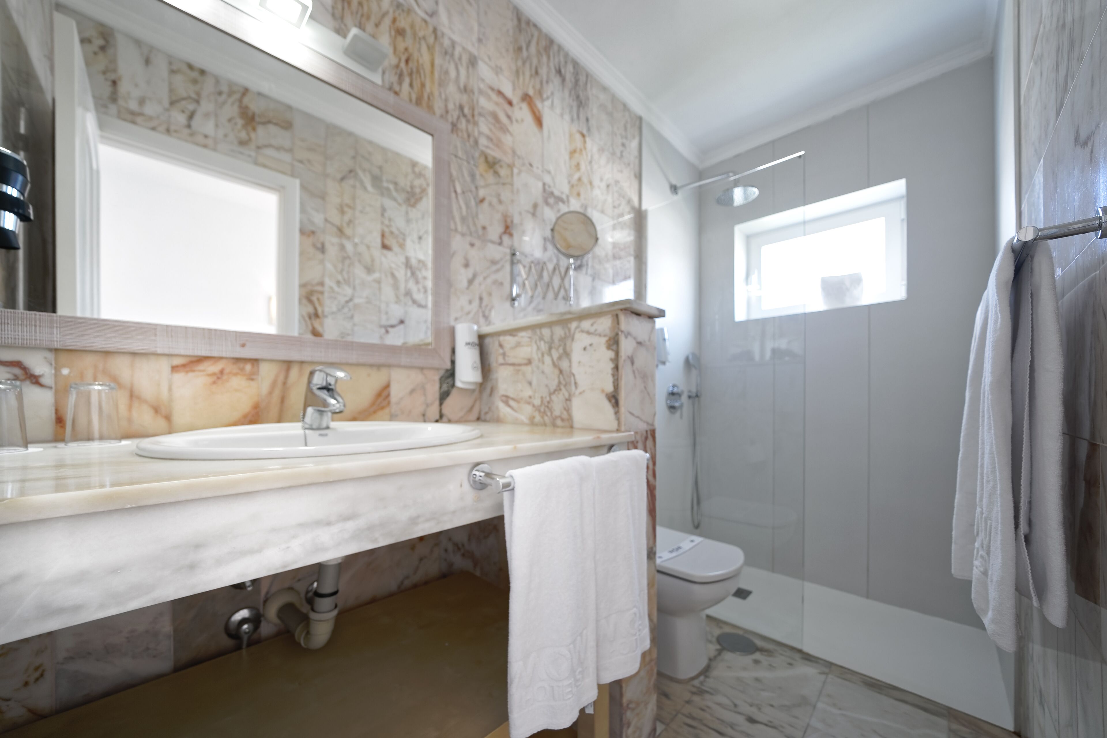 Un baño con lavamanos de mármol, inodoro y zona de ducha.