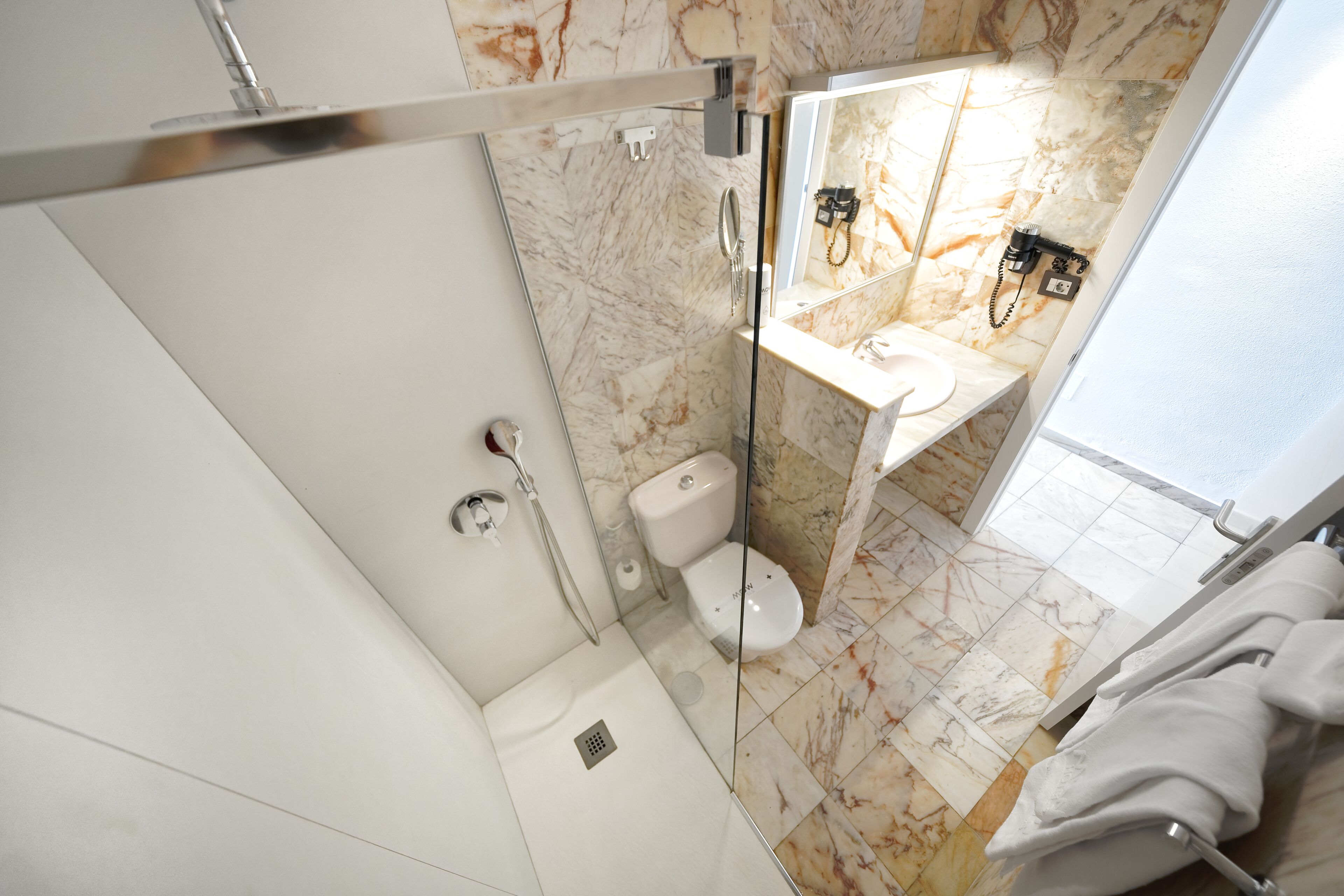 Un baño moderno con ducha envuelta en vidrio, inodoro y lavamanos con resguardo de mármol.