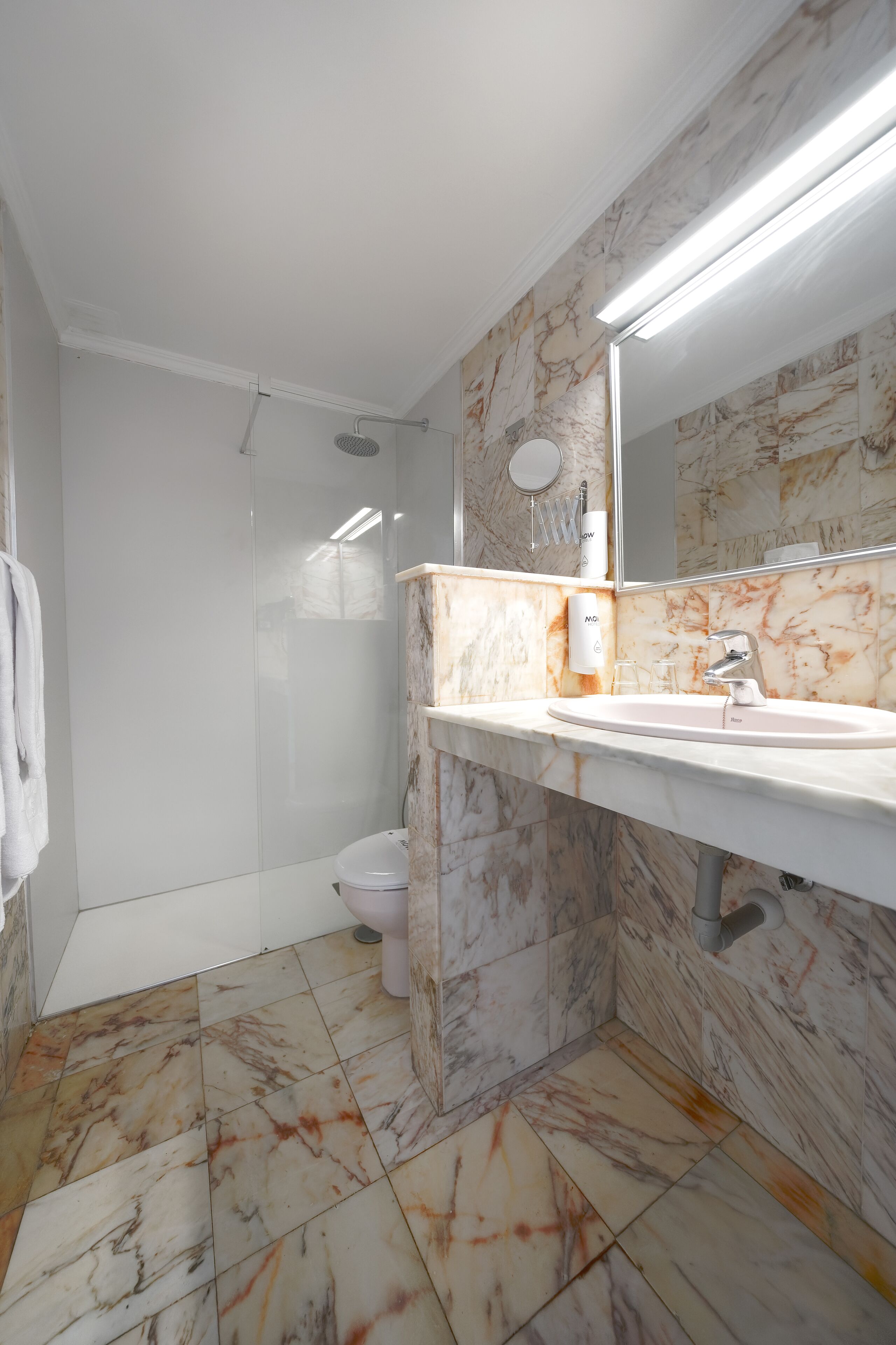 A modern bathroom with a marble floor, a white sink, a mirror, and a shower.