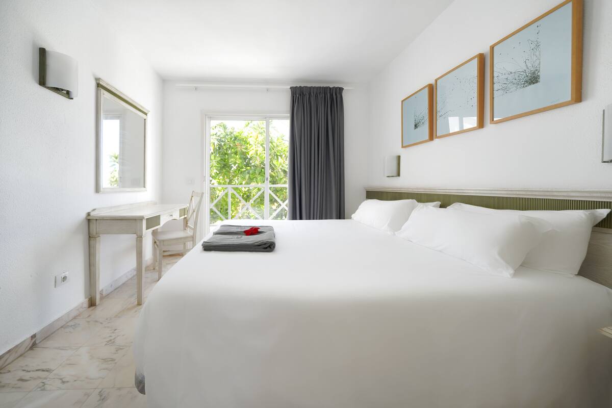 Une chambre d’hôtel avec un grand lit, un bureau et une chaise. Il y a trois tableaux encadrés accrochés au mur.