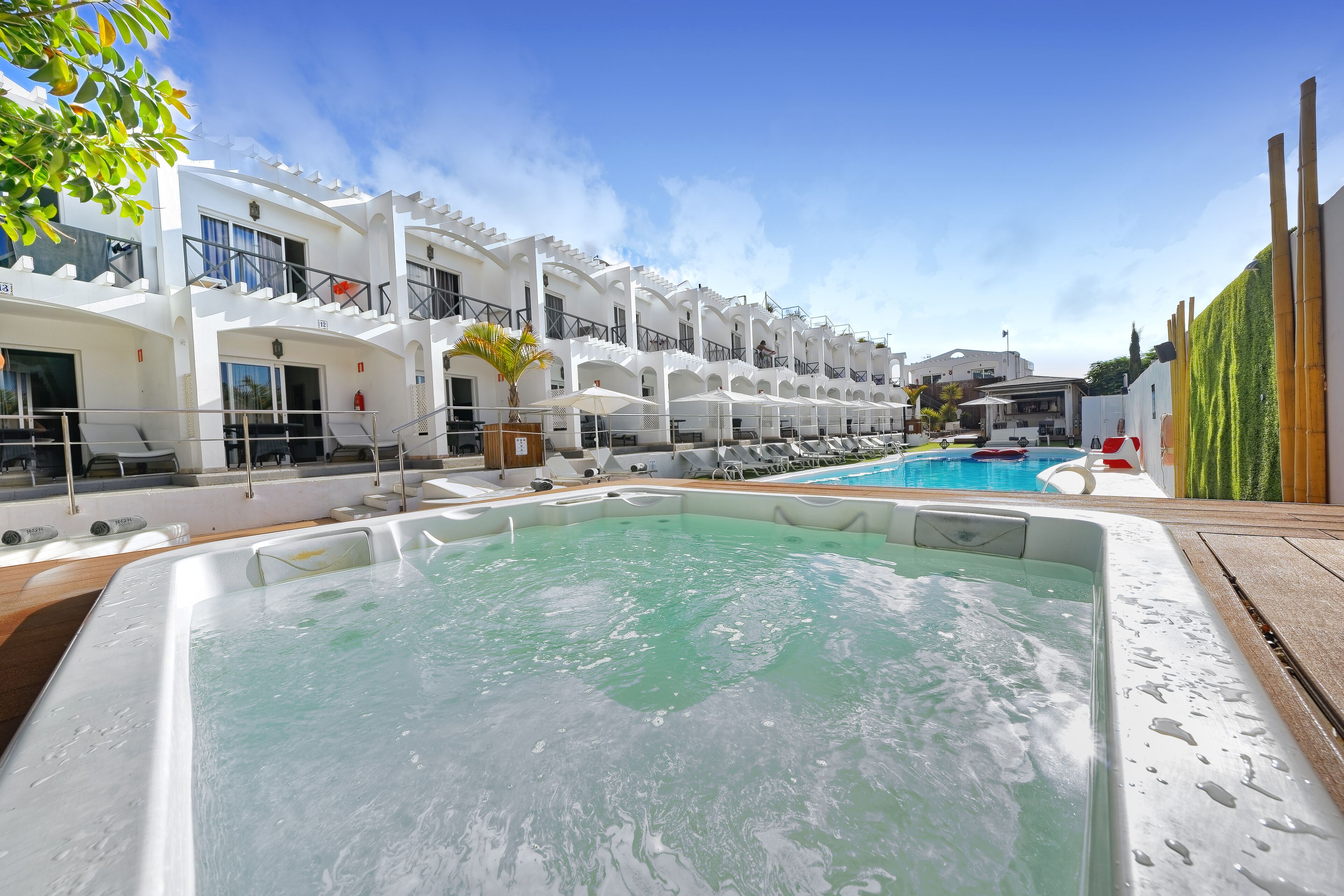 A hotel with a pool, outdoor seating, and a hot tub.