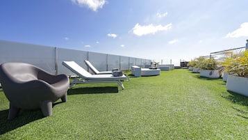 Una terraza en la azotea con césped artificial, sillones de descanso y plantas en macetas.