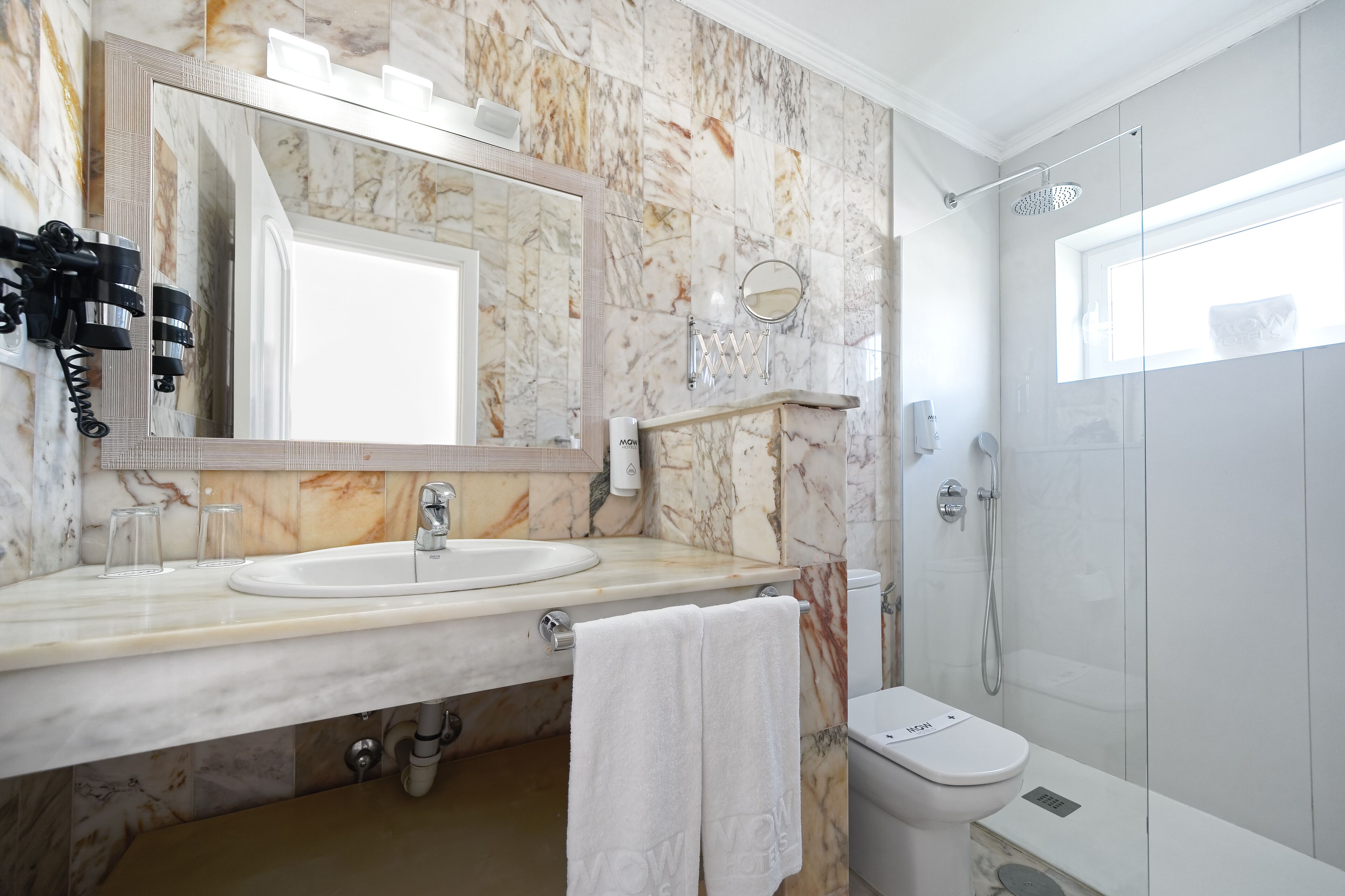 Un baño con tocador de mármol, un espejo grande, inodoro y ducha con mampara de vidrio.