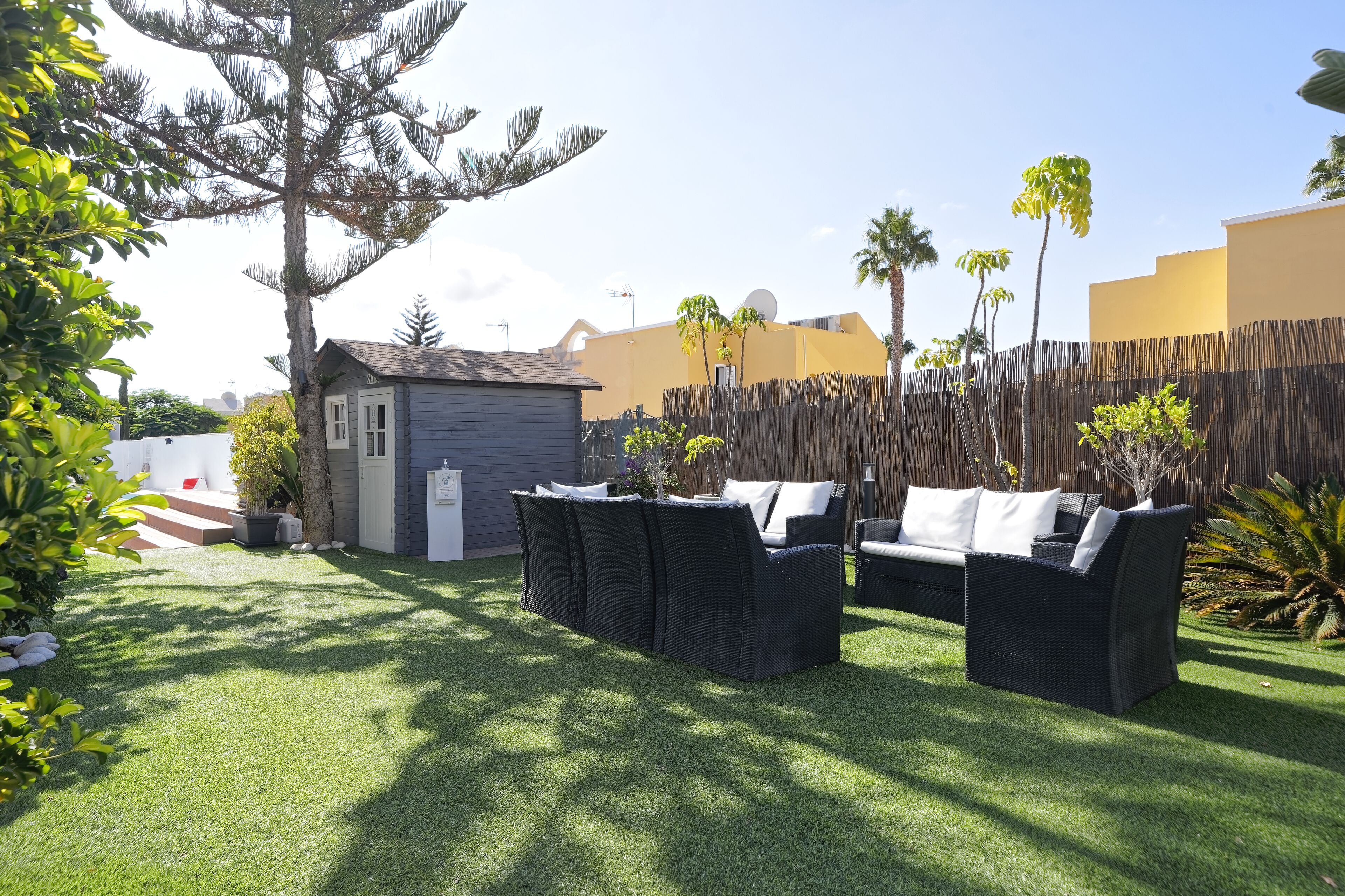 A backyard with artificial grass, a small shed, a wicker sofa set, and a wooden fence.