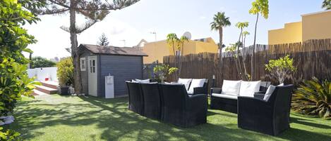 A backyard with artificial grass, a small shed, a wicker sofa set, and a wooden fence.