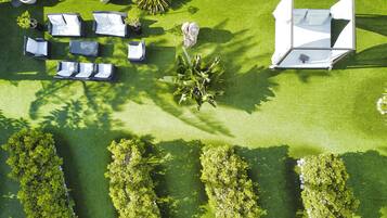 Vue aérienne d’un jardin bien entretenu, avec un espace patio aménagé comprenant des meubles d’extérieur, une petite fontaine et des haies soigneusement taillées.