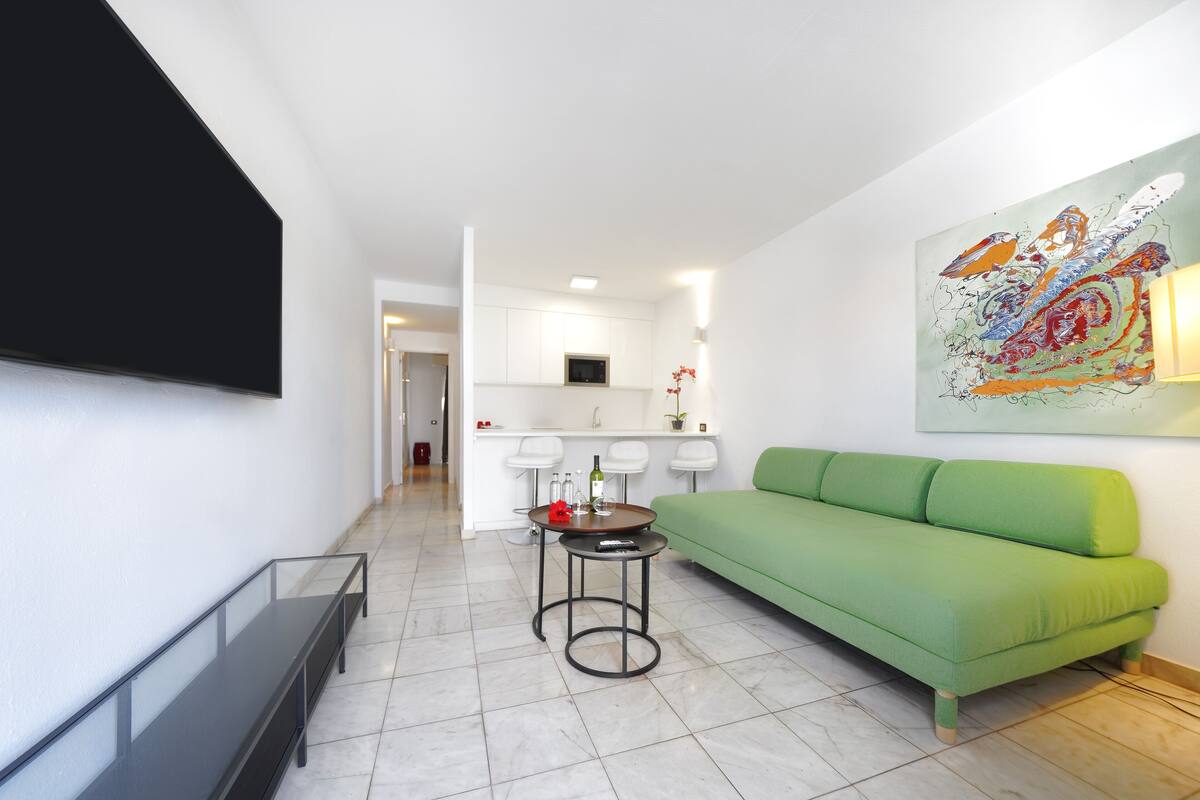 Un salon moderne avec un canapé vert, une petite table ronde et un téléviseur fixé au mur.
