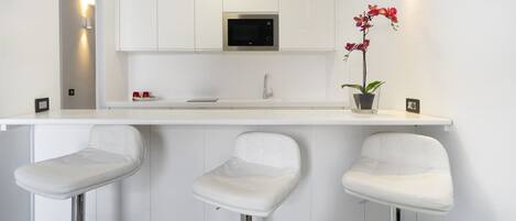 Una cocina moderna con armarios blancos, un microondas integrado y tres taburetes blancos.