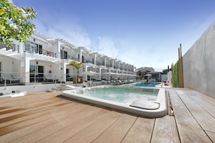 A poolside area with a hot tub, lounge chairs, and a pool.
