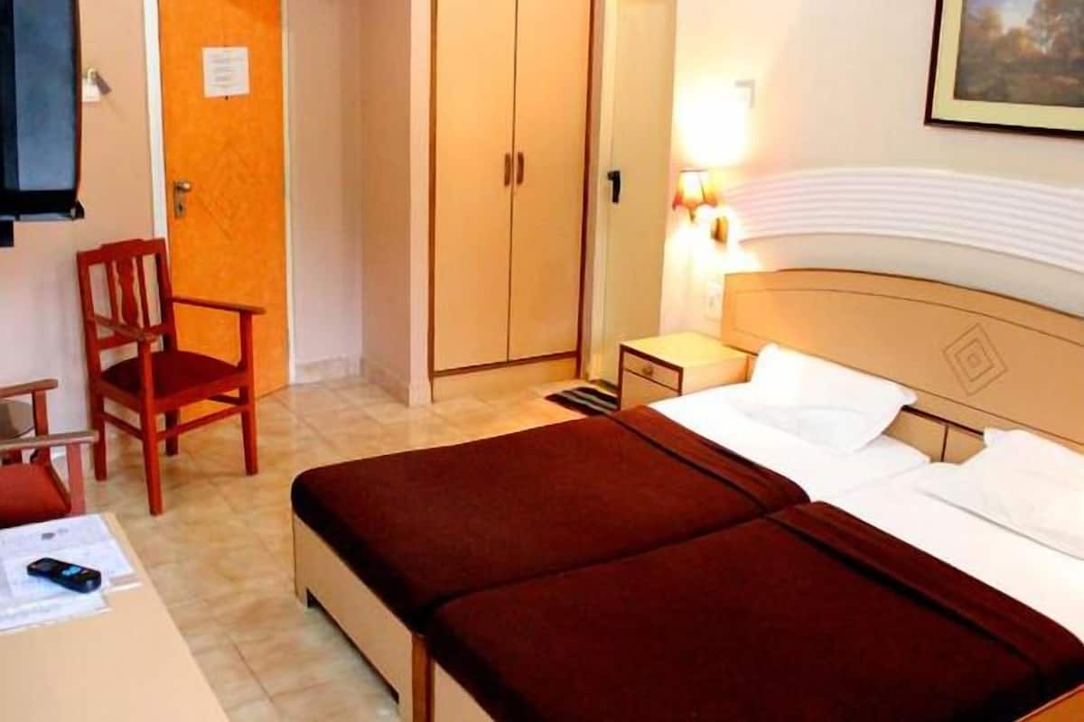 Ein Hotelzimmer mit Bett, Sessel, Schrank und Nachttisch mit Lampe.