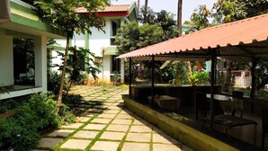 Un patio con un sendero de baldosas, una zona de estar cubierta y un edificio con tejado rojo.