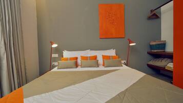 Una cama bien hecha con ropa de cama blanca y naranja, dos lámparas de noche y una obra de arte naranja colgada en la pared.