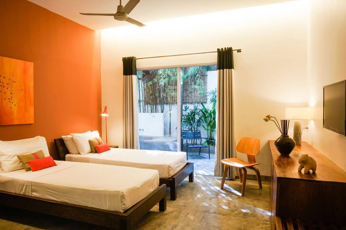 A hotel room with two beds, a desk, a chair, a TV, and a view of the outdoors.