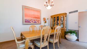 A dining room with a wooden table and chairs, a chandelier, a cabinet, and a painting on the wall.