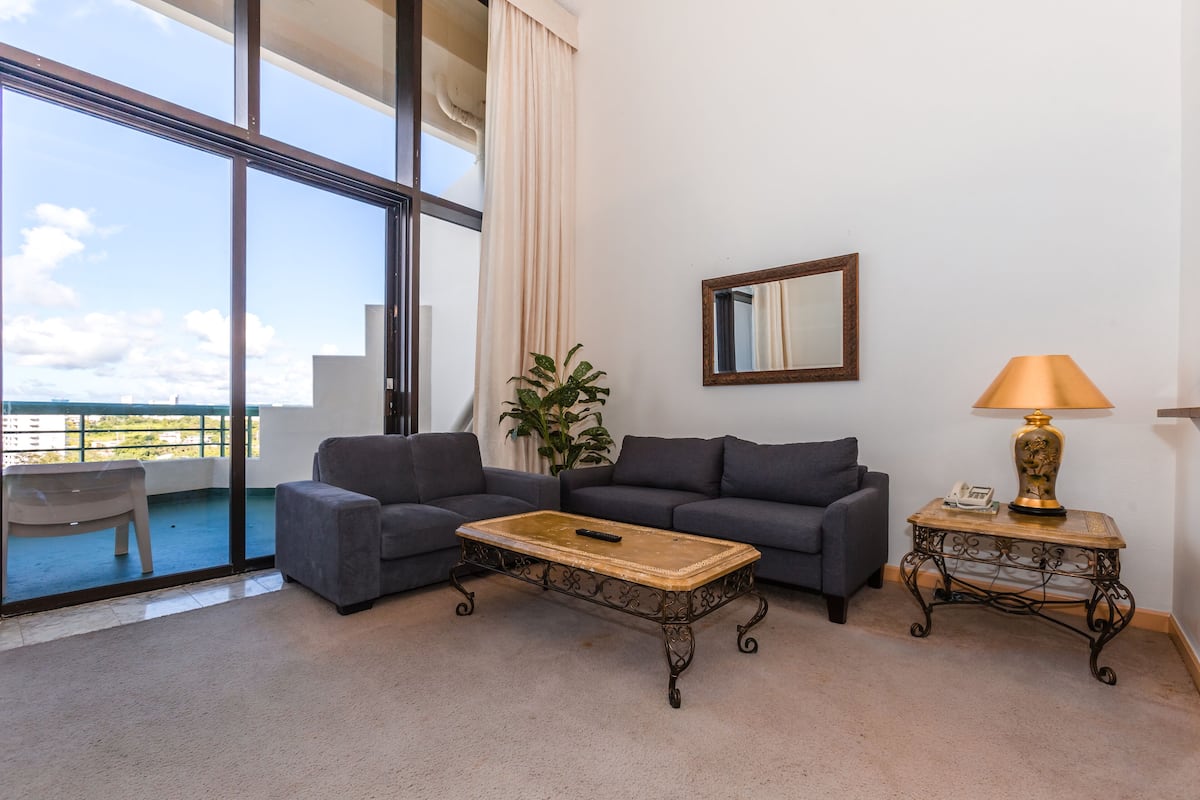 A living room with a sofa, a coffee table, a lamp, a mirror, and a potted plant.