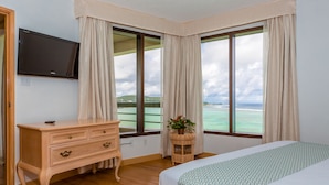A hotel room with a bed, a dresser, a television, and large windows with curtains. - Alupang Beach Tower (Tamuning)