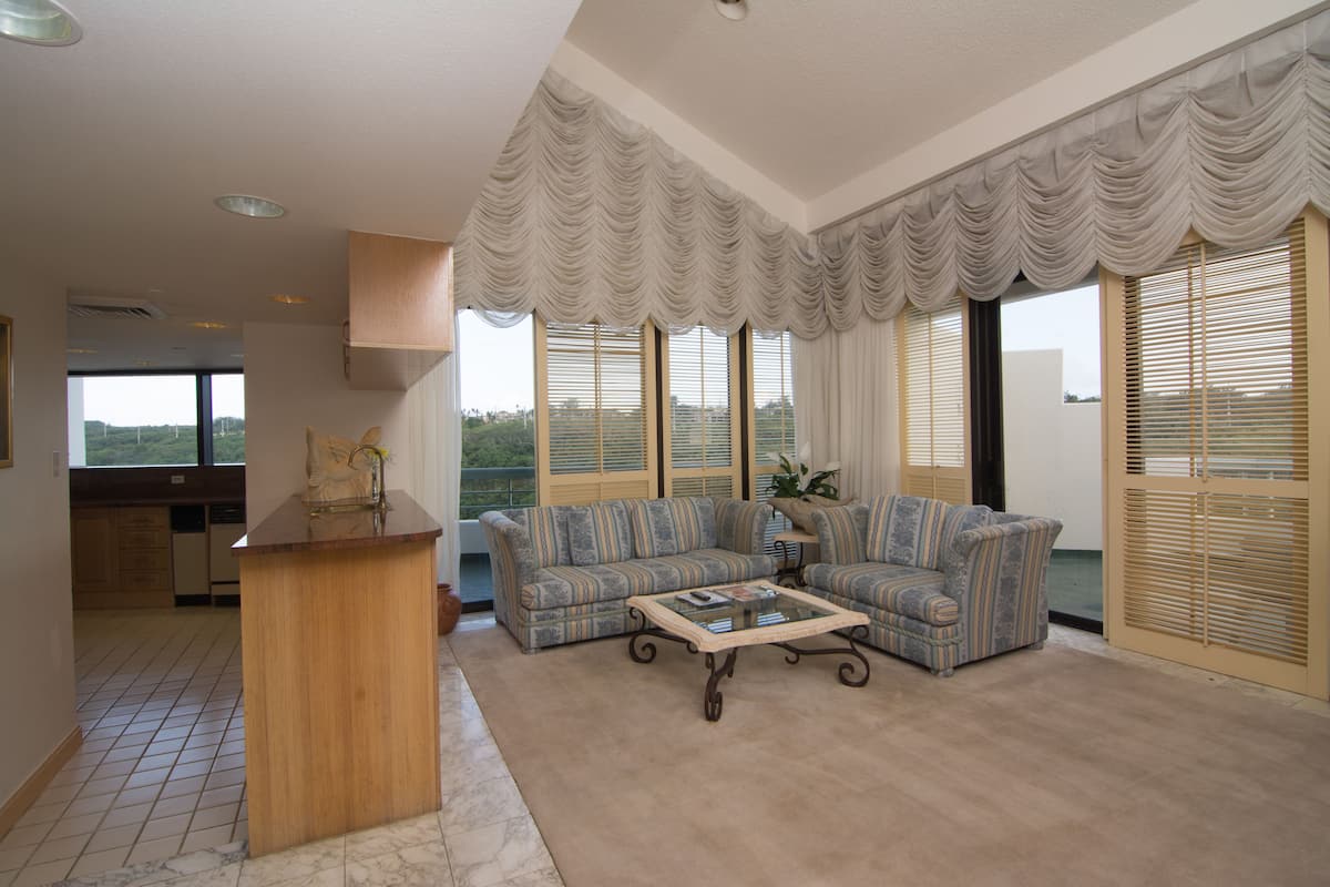A spacious living room with a large sofa set, a wooden coffee table, and a kitchen area visible through an open door.