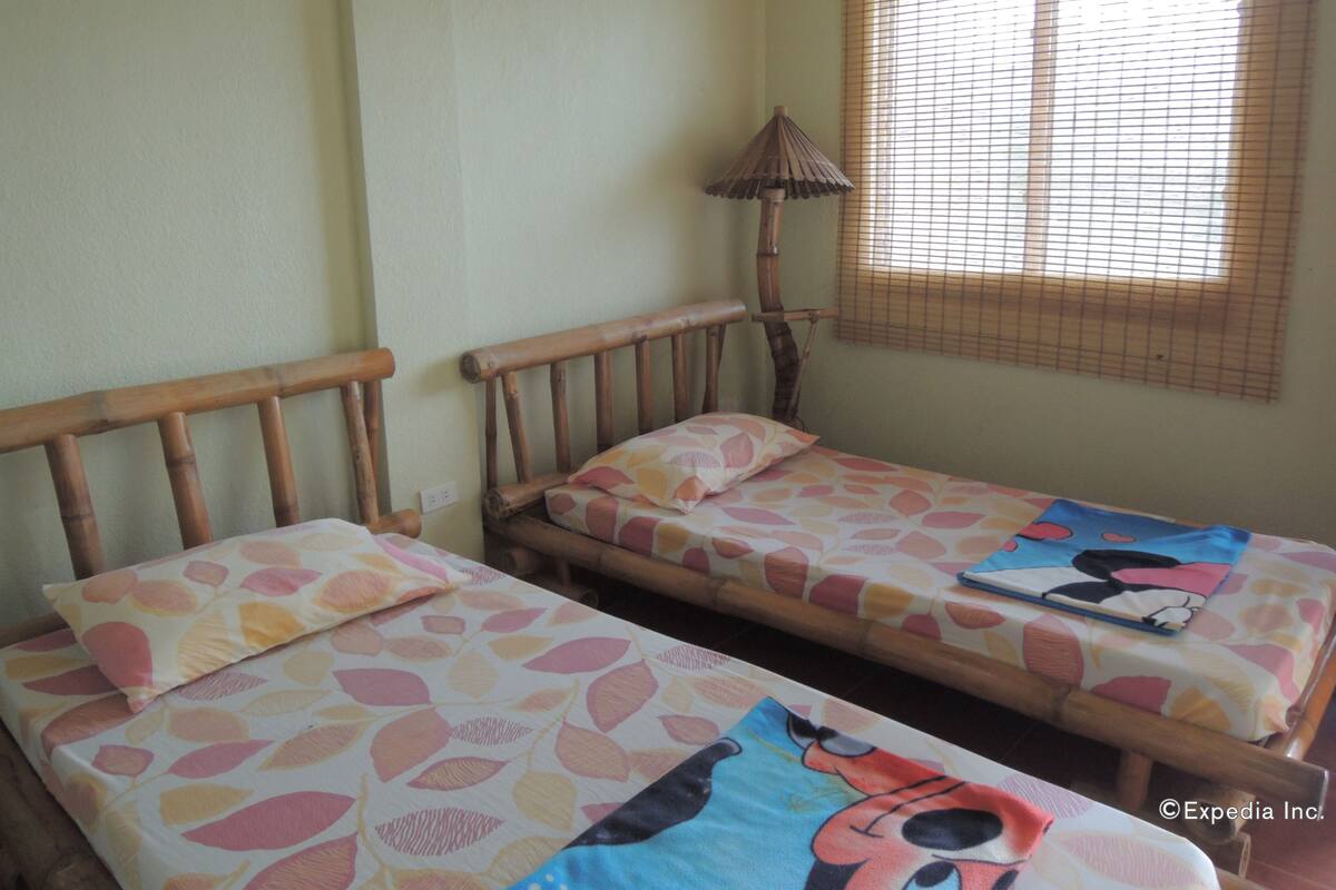 A room with two wooden beds with colorful bedding, a small table, and a lamp.