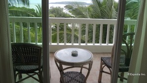 A balcony with a glass table and two wicker chairs, overlooking a tropical landscape with palm trees and a body of water. - Moalboal Beach Resort (Moalboal)
