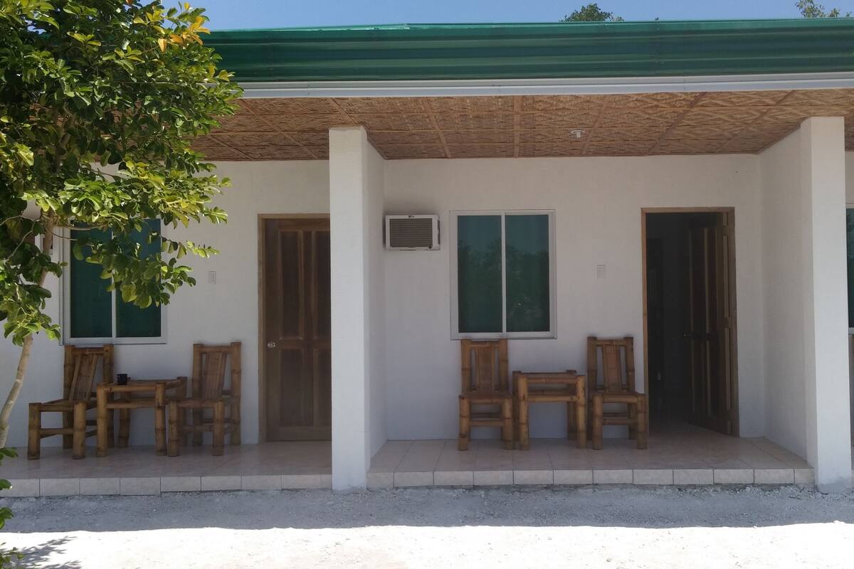 A building with a covered porch, wooden chairs, and a green roof.