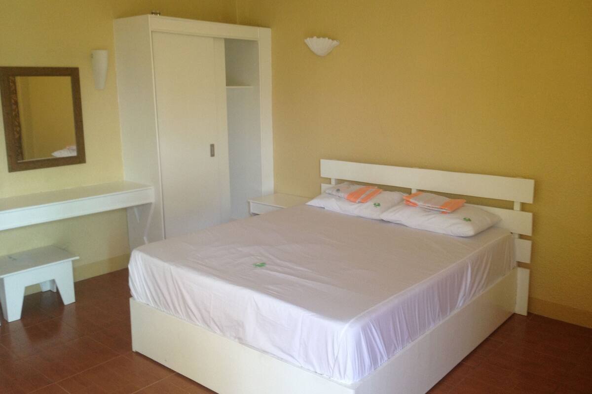A bedroom with a bed, a wardrobe, a bedside table, and a mirror.
