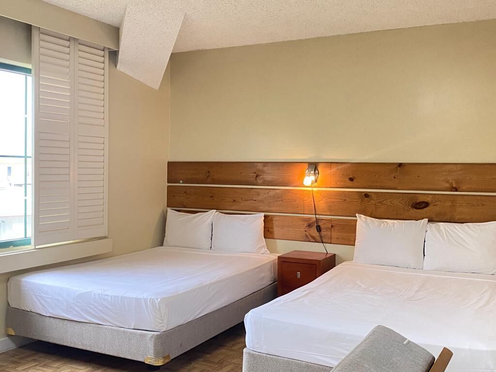 A room with two beds, a wooden headboard, a nightstand, and a window with shutters.