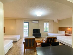 A hotel room with two single beds, a TV, a small table, and a seating area with chairs.