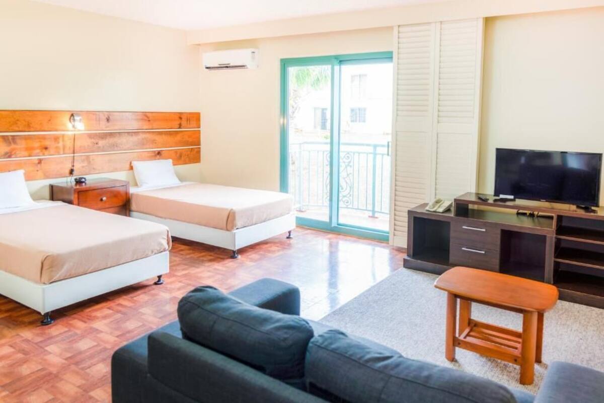 A hotel room with two beds, a TV, a desk, and a balcony.