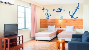 A hotel room with two beds, a TV on a wooden stand, a small table, and a blue sofa. - Garden Villa Hotel (Tamuning)