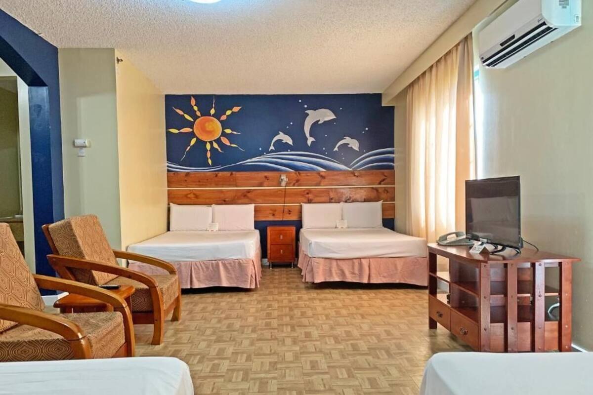 A hotel room with two beds, a TV, a desk, and a mural of a sun and dolphins.