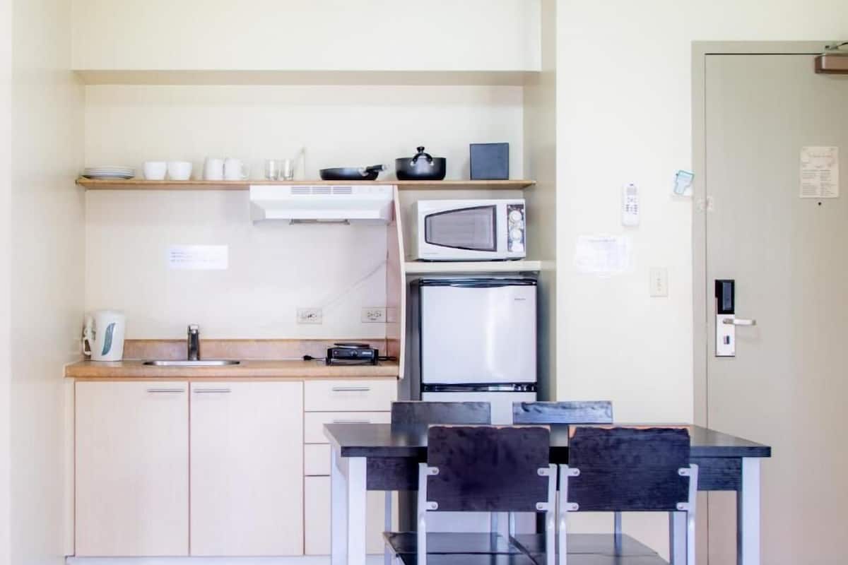 A compact kitchenette with a microwave, a small refrigerator, a sink, and a dining table with chairs.