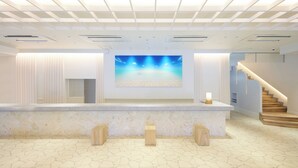 A reception area with a large digital screen displaying a beach scene, a marble reception desk, and a staircase leading to upper floors. - Pricia Resort Yoron (Yoron)