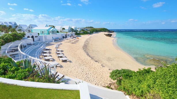 A beach resort with a curved walkway leading to a sandy beach, clear turquoise waters, and white buildings with blue roofs. - Pricia Resort Yoron (Yoron)
