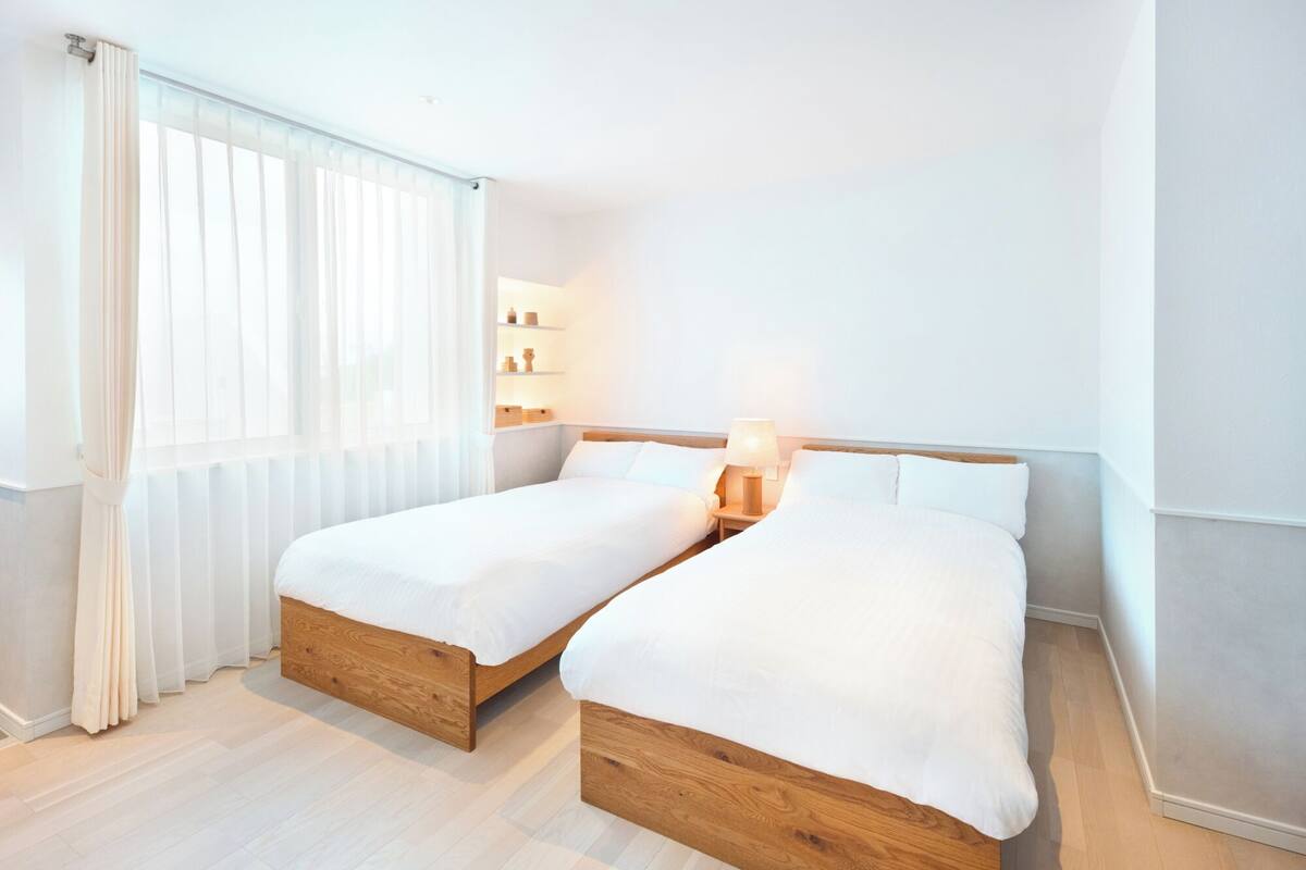 A double bed room with a wooden headboard, a bedside table with a lamp, and a window with sheer curtains.