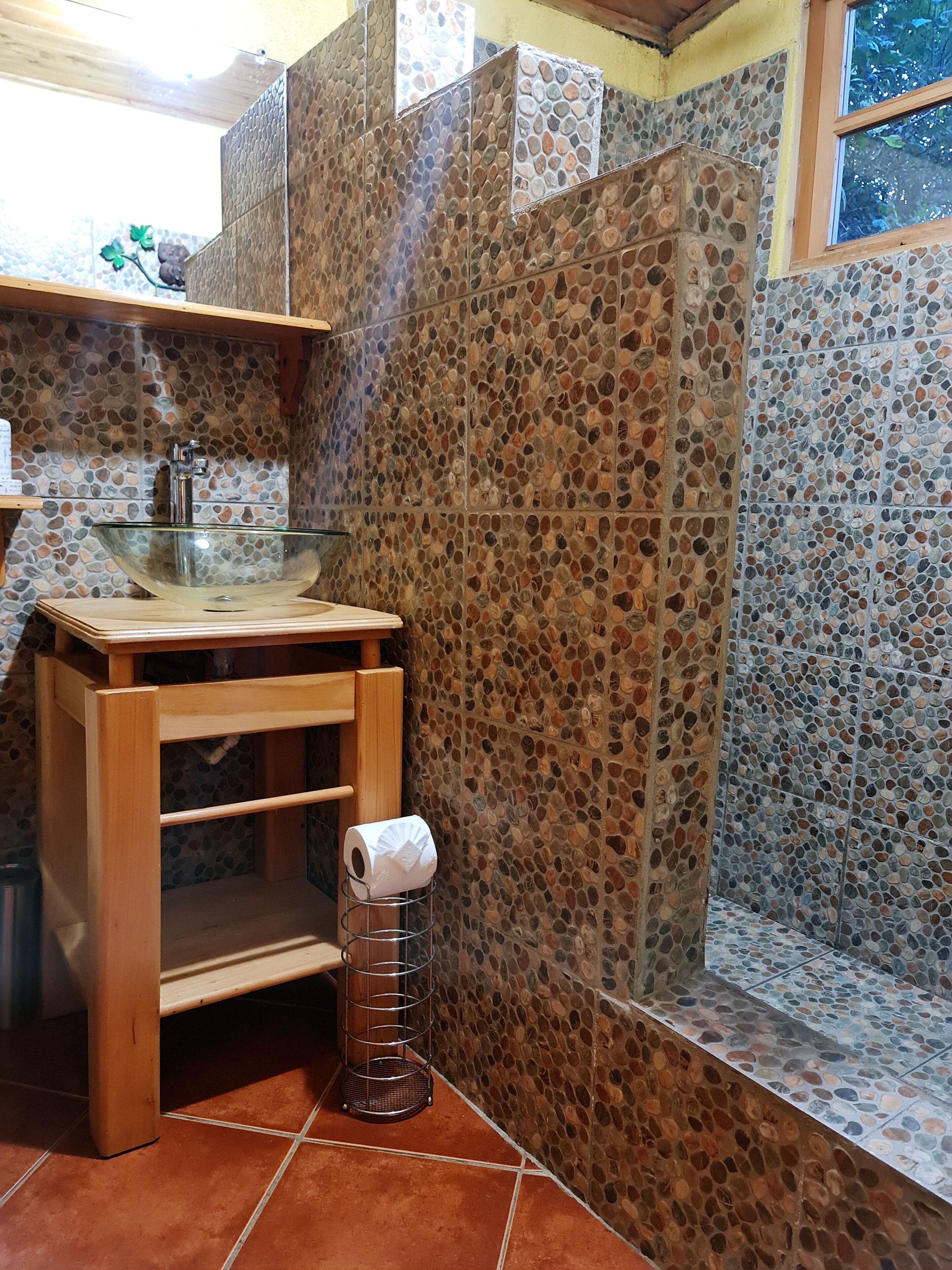 A bathroom with a stone mosaic wall, a glass sink, and a wooden vanity.