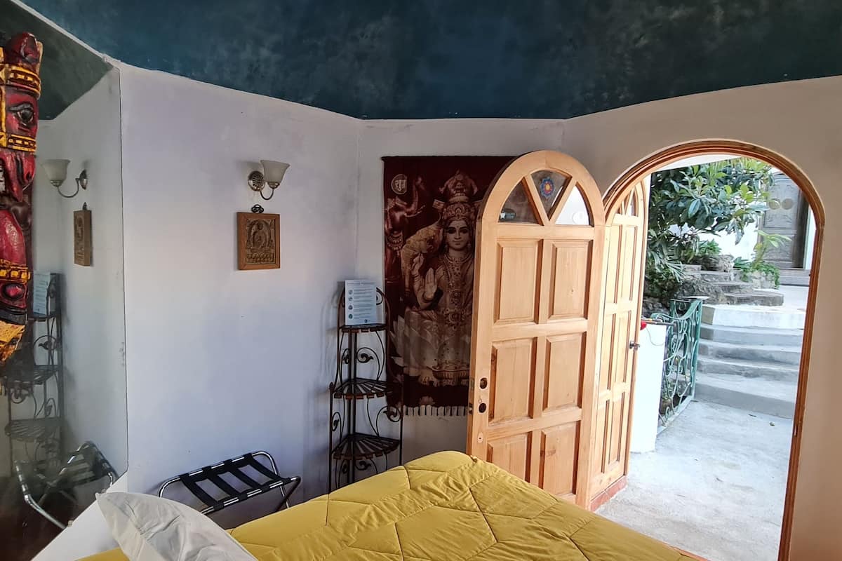 Ein Zimmer mit einem Bett, einer Holztür, einem Spiegel und einer Wand mit einem religiösen Wandgemälde.