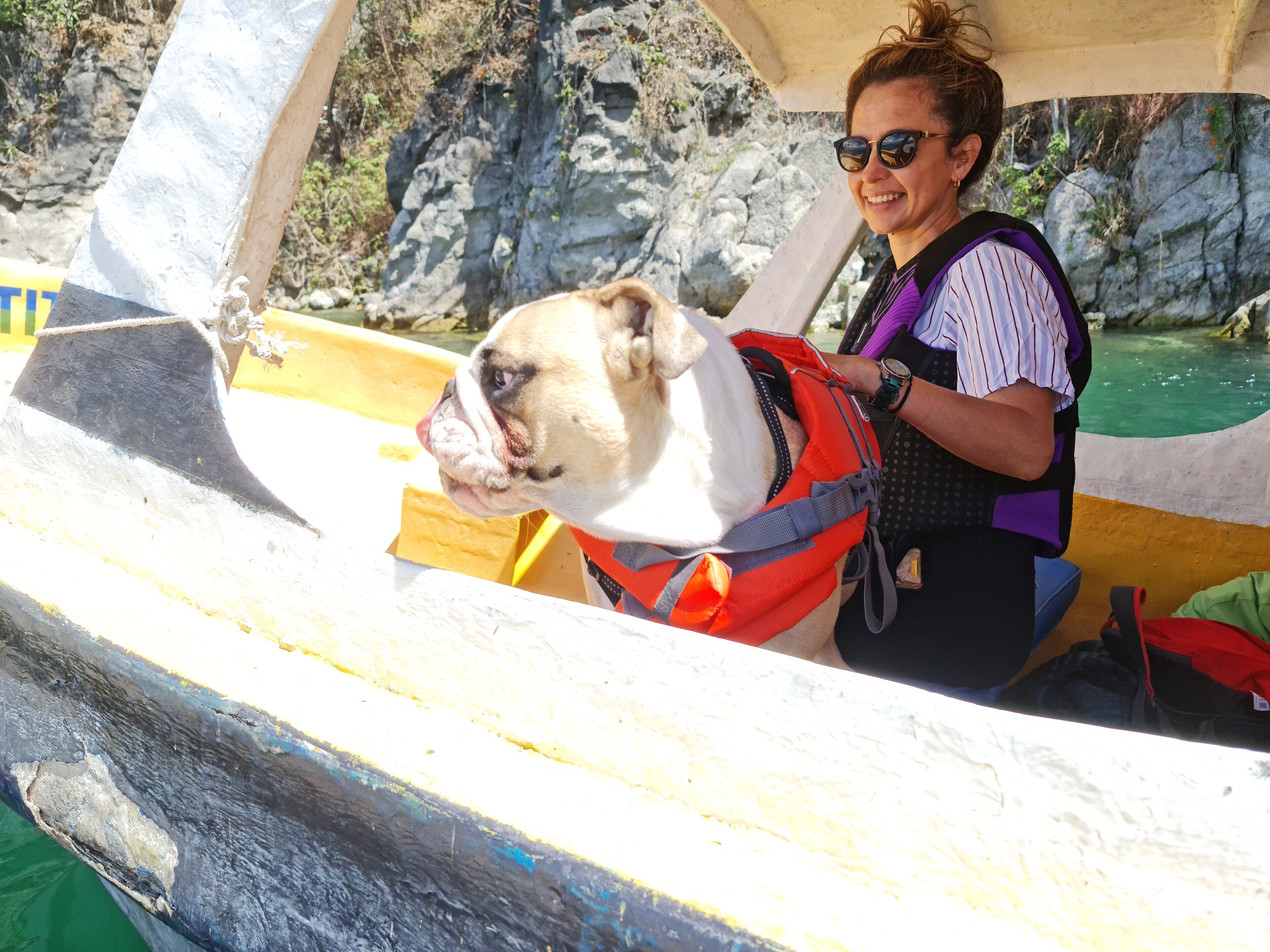A person in a boat wearing a life jacket, with a dog in a life jacket.