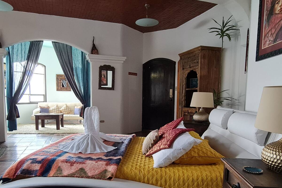 Ein geräumiges Wohnzimmer mit einem großen Bett, einer Couch und einem Couchtisch. Durch eine Tür ist ein Balkon zu sehen.