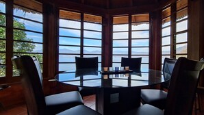 A round glass table with four chairs in a corner room with large windows. - Atitlan Oasis Eco Hotel and Spa Kaalpul (San Antonio Palopo)
