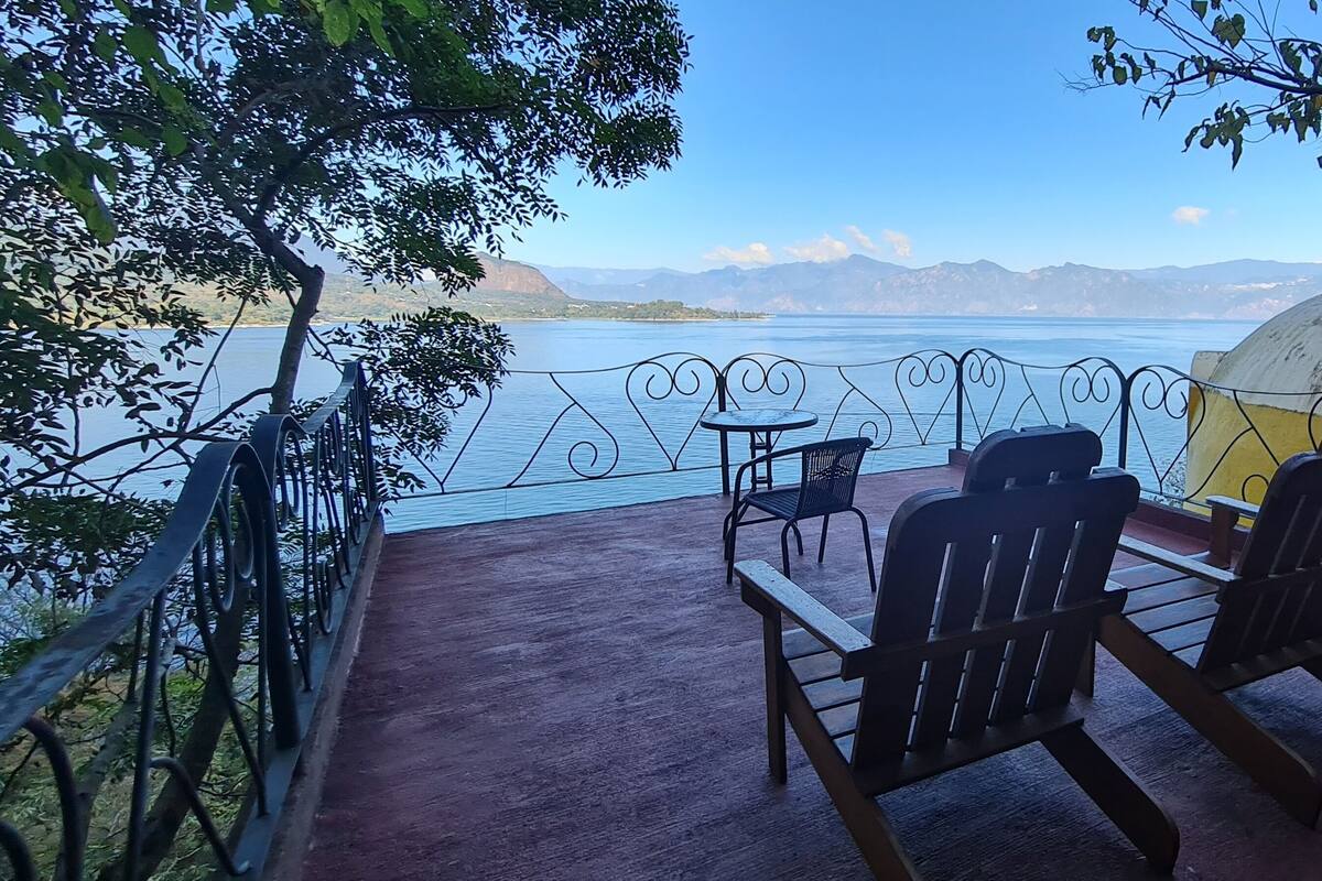 Eine Terrasse mit Tisch und Stühlen mit Blick auf einen See, im Hintergrund Berge und in der Nähe eine Kuppelstruktur.
