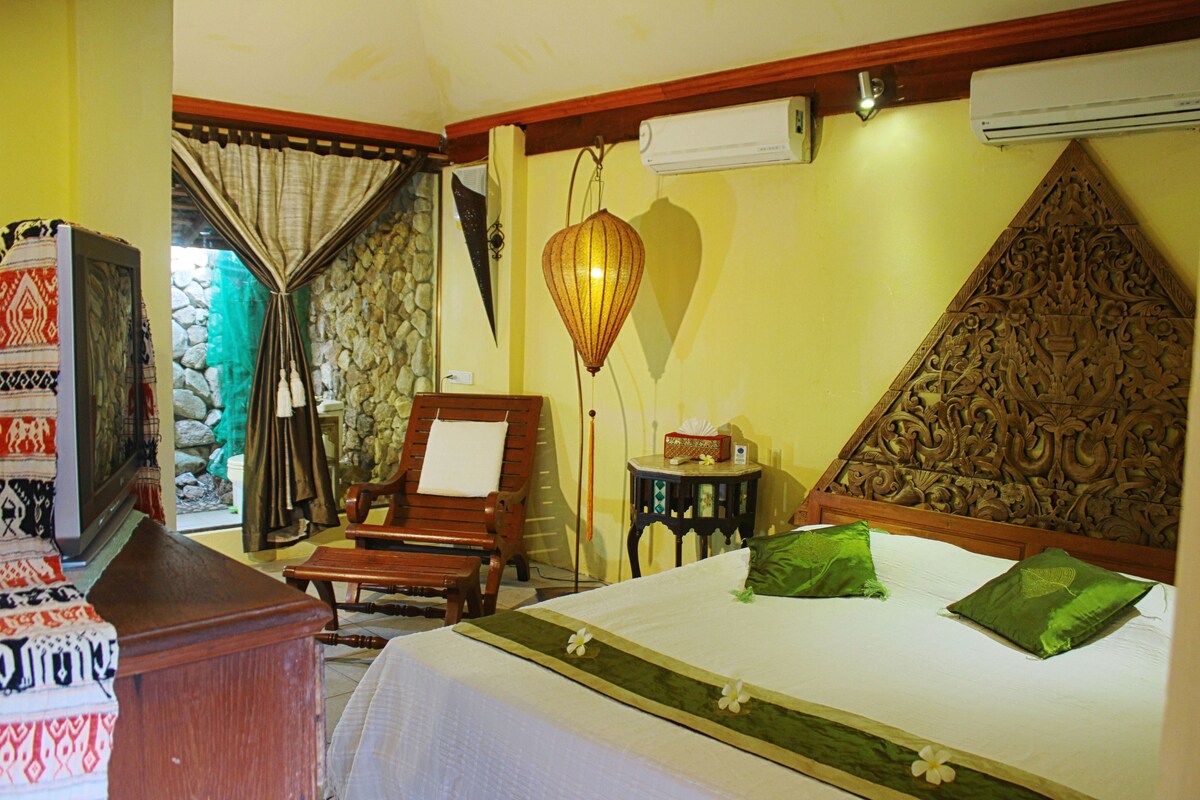 A hotel room with a bed, a wooden chair, a small table, and a television.