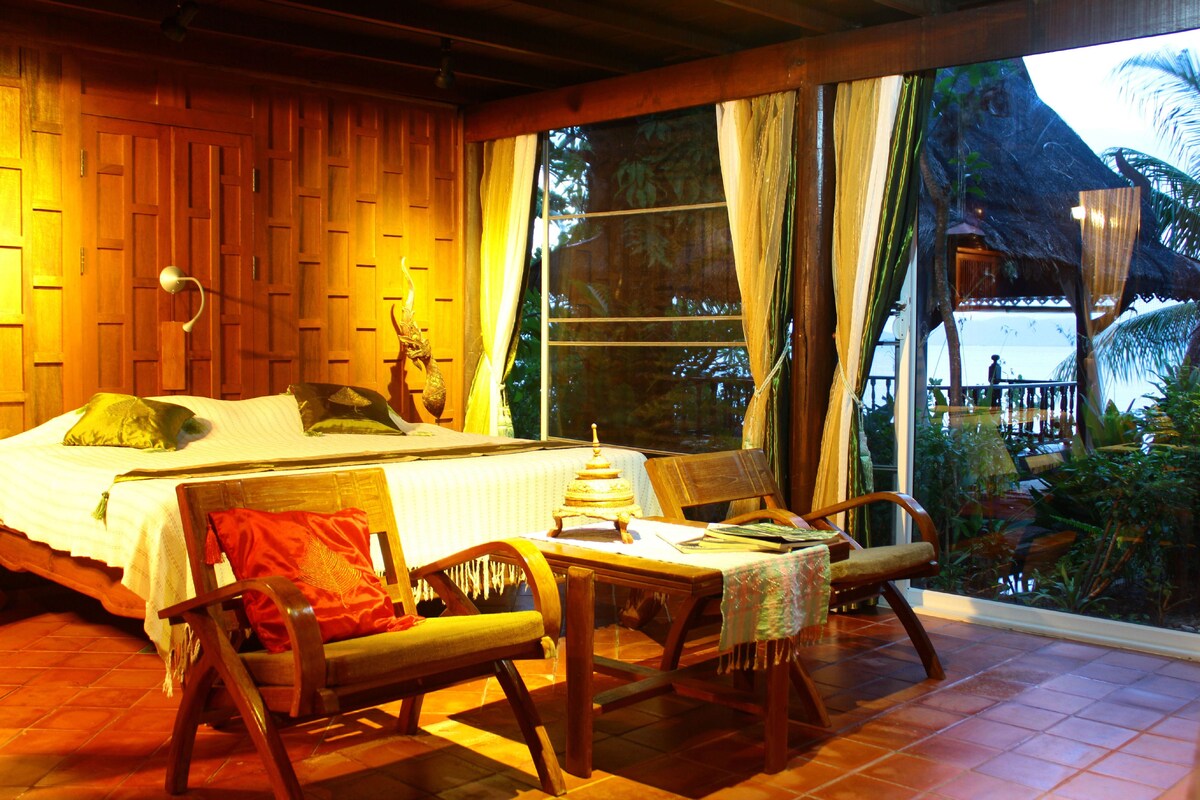 A bedroom with a bed, two chairs, a table, and a view of the outdoors.